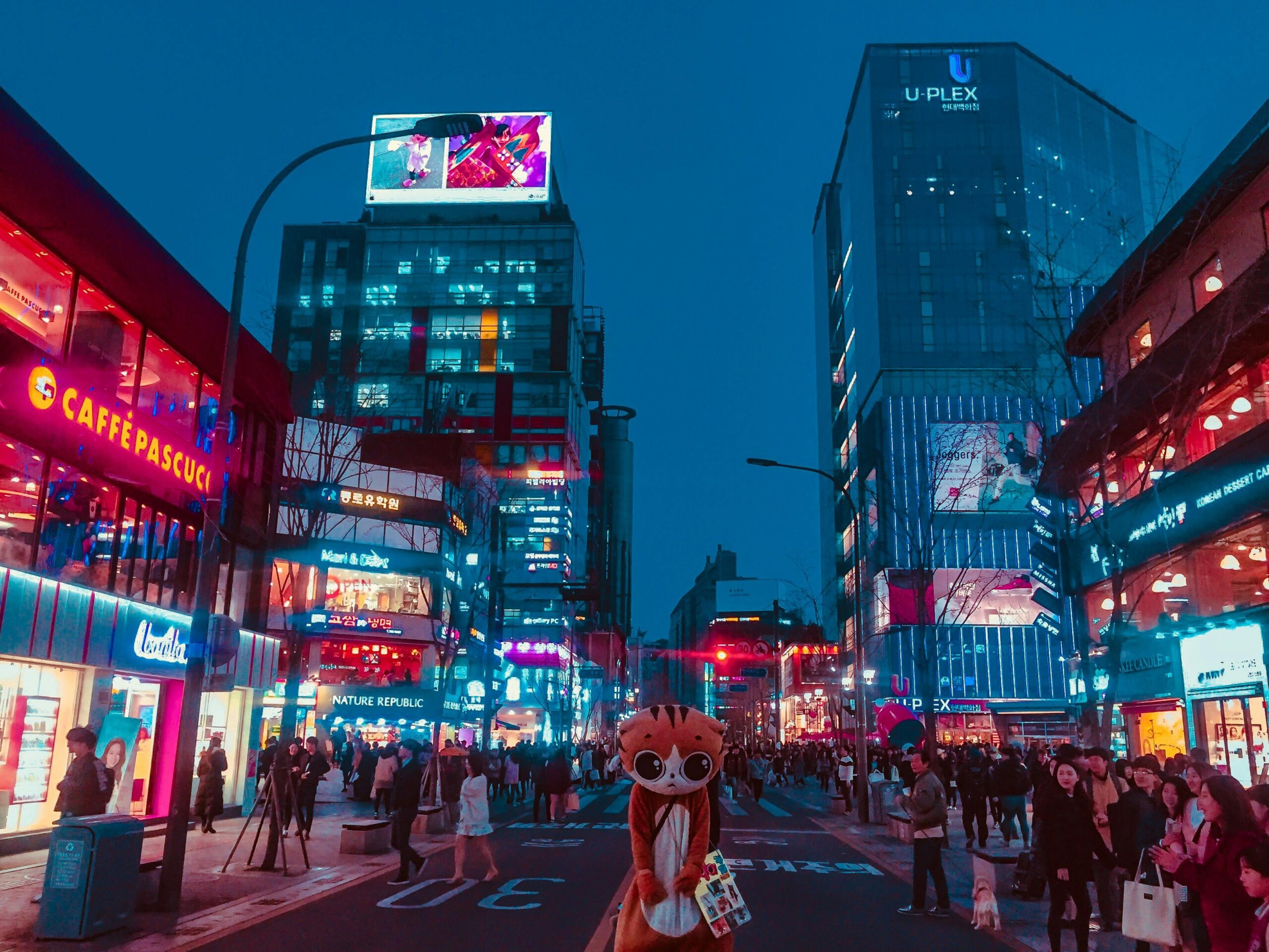 A street in Myeongdong, Seoul at night showcasing neon lights and people shopping.