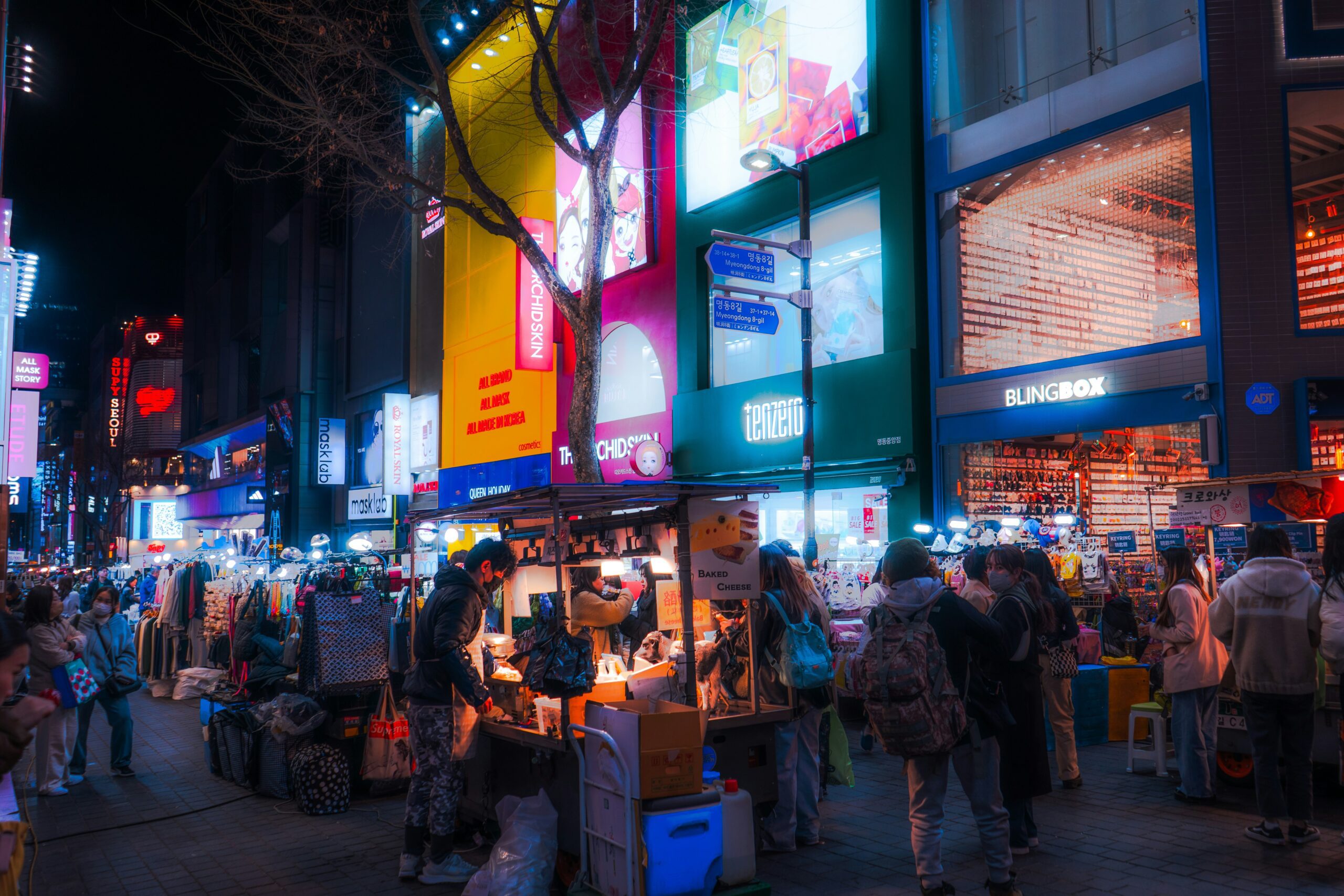 A street in Myeongdong at night, with shoppers and street food carts.