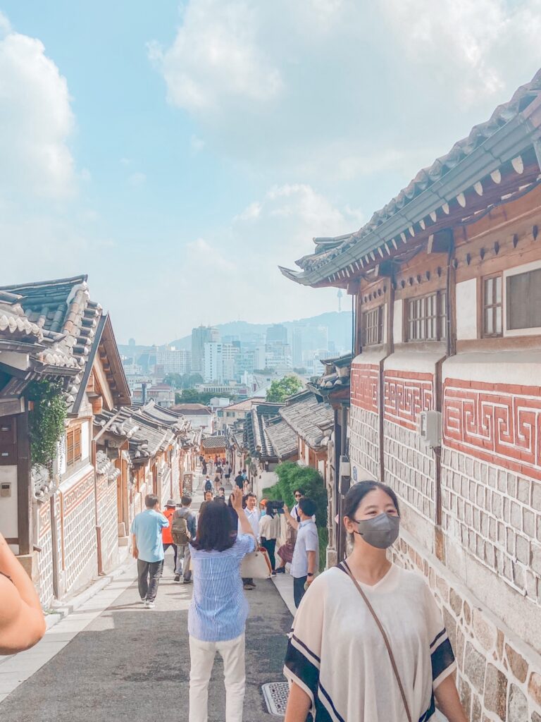 Bukchon Hanok Village in Seoul on a sunny day with tourists and Namsan Tower in the background.