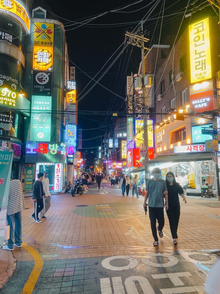 A street in Hongdae at night with neon lights.