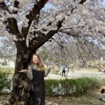 A woman standing below a cherry blossom tree at Yeouido Hangang Park