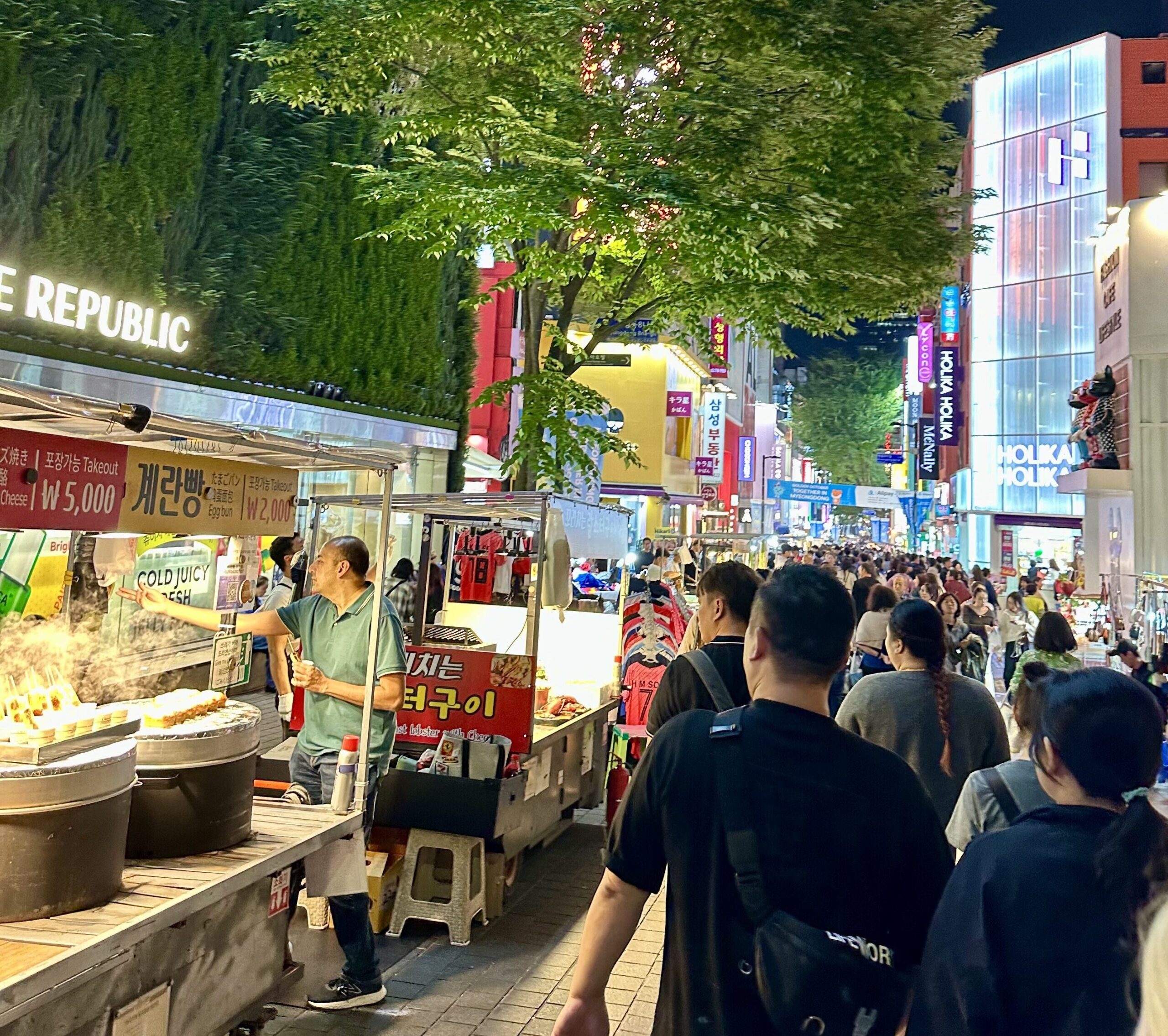 A crowd walking through Myeongdong Walking Street, surrounded by street food carts.